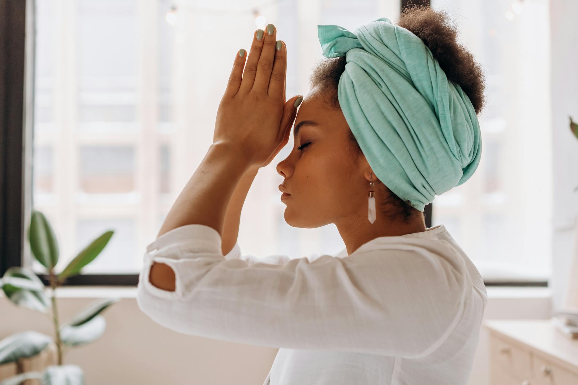 A woman in a green head wrap with her palms pressed together at her forehead and her eyes closed