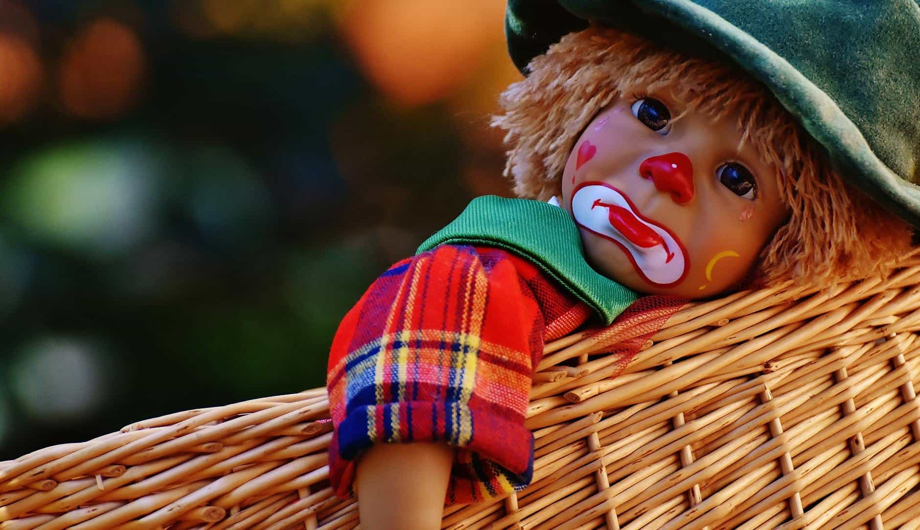 A sad-faced clown doll with a pacifier, lying in a wicker basket